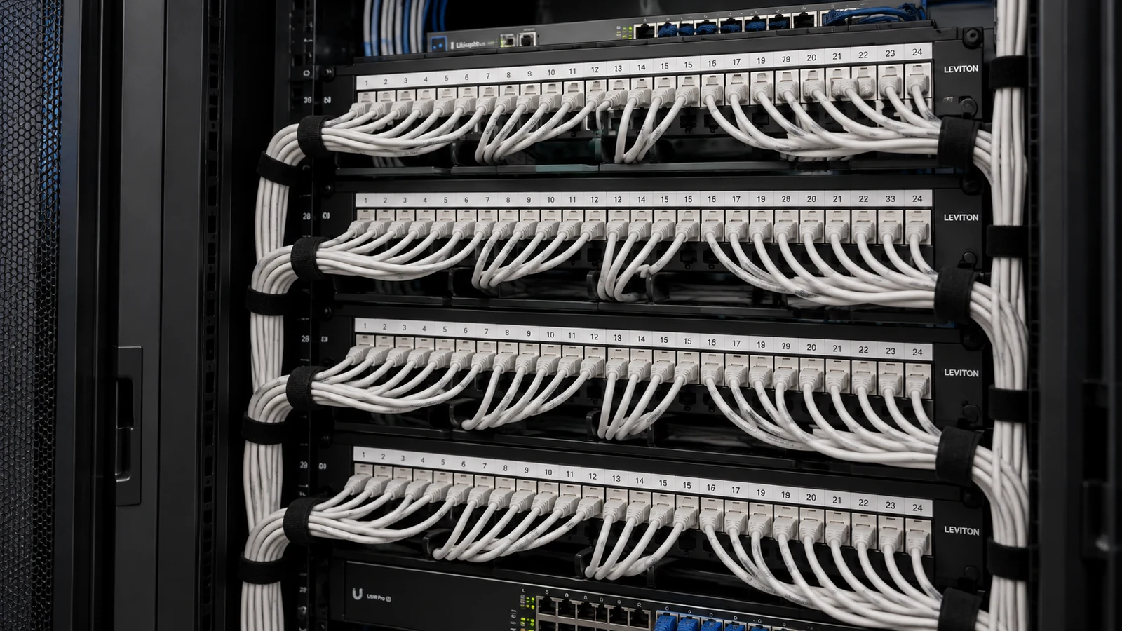 Network rack with four patch panels, organized white Ethernet patch cords, and rack-mounted switches.