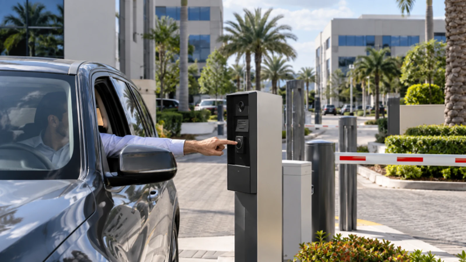 Driver presenting an access card to a commercial gate reader beside a barrier arm.