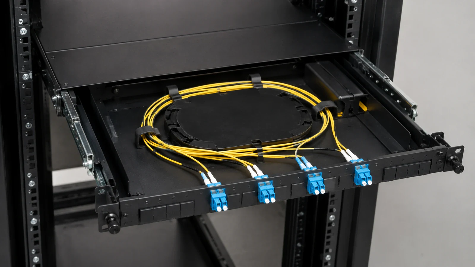 Open rack-mounted fiber drawer with protected yellow slack and four duplex optical connections.