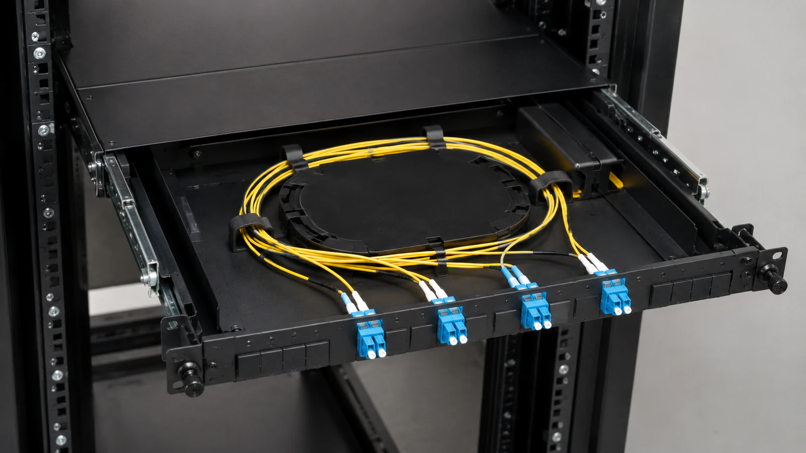 Open rack-mounted fiber drawer with protected yellow slack and four duplex optical connections.