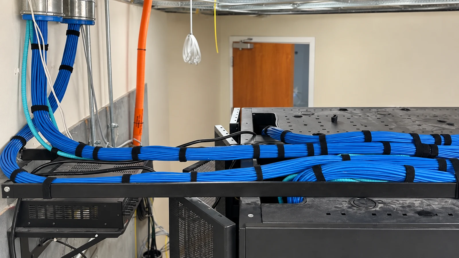Blue data-cable bundles secured with hook-and-loop straps along a ladder rack in a telecom room.