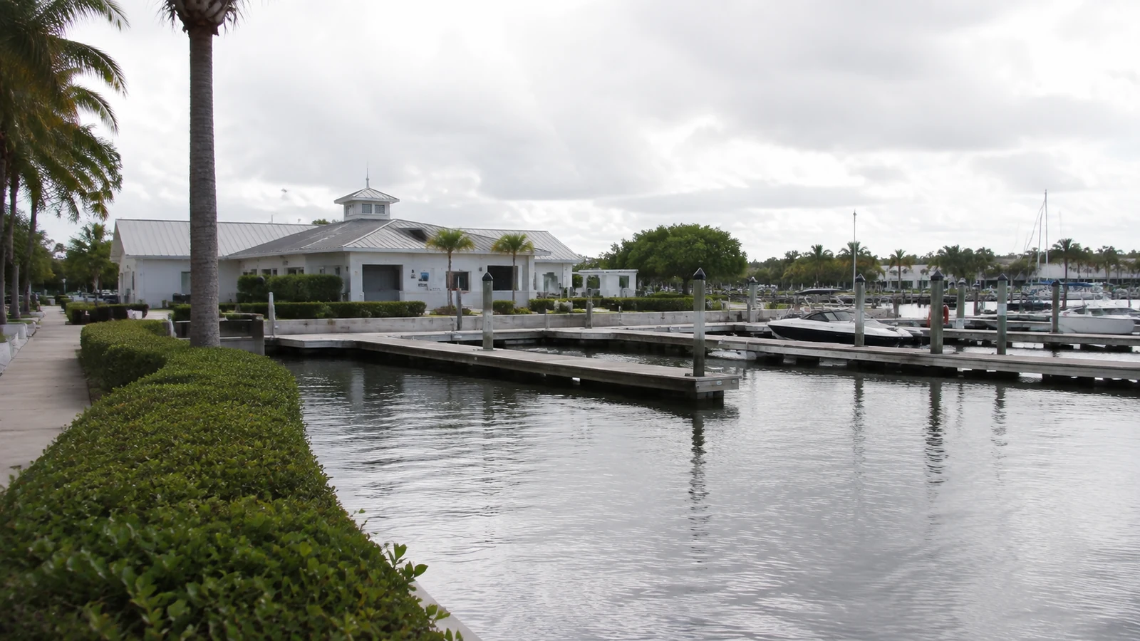 Florida marina basin with floating docks, moored boats, a waterfront service building and a paved vehicle approach.