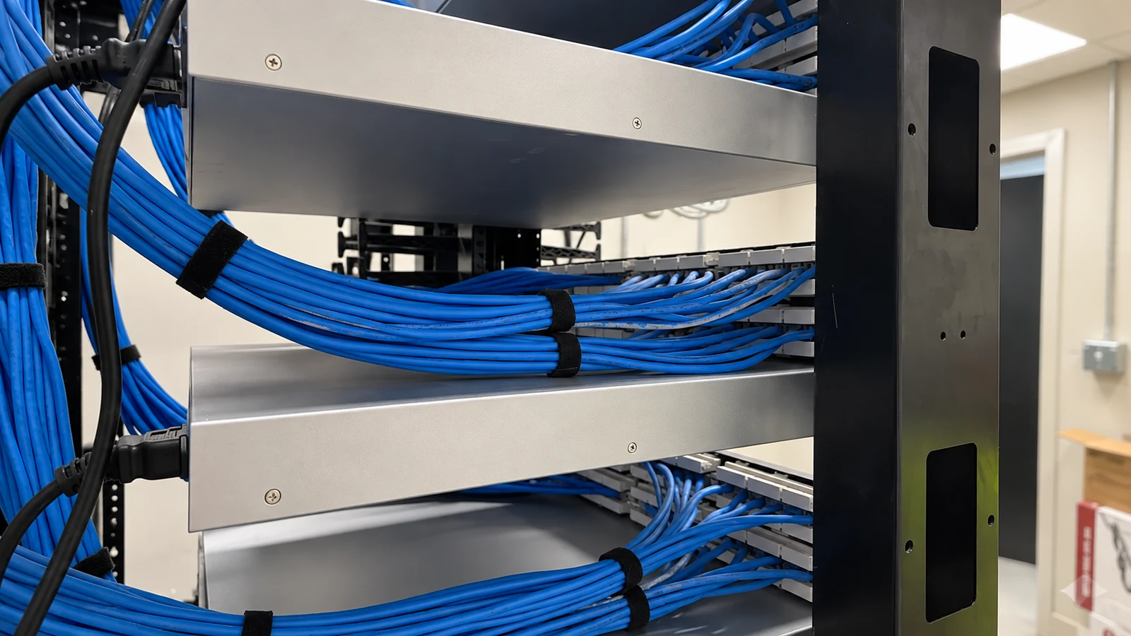 Blue copper cables organized behind rack-mounted equipment with visible supports and straps.
